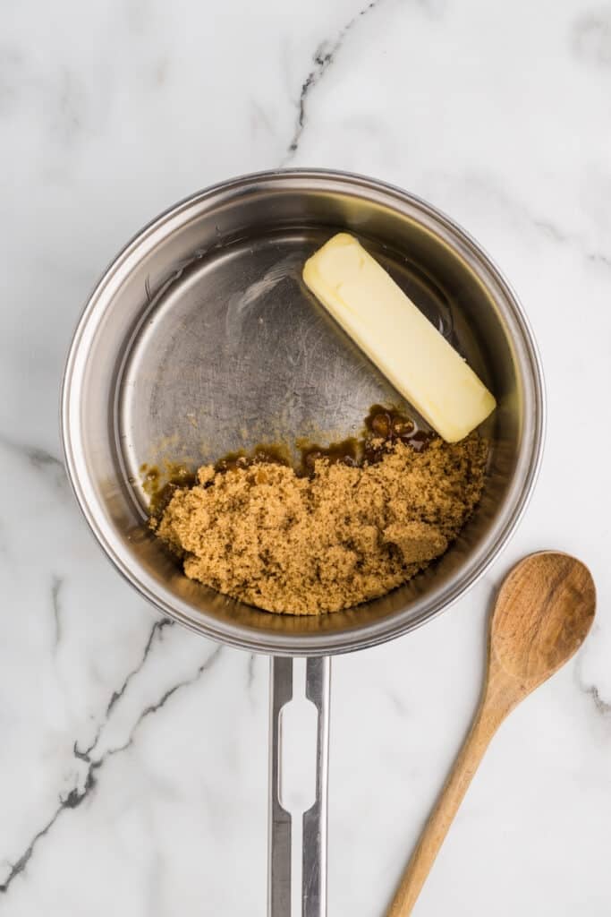 Butter and brown sugar in a saucepan with a wooden spoon beside it.