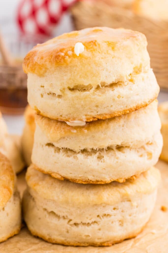 A stack of three thick, golden biscuits with visible flaky layers and a small spot of melted butter on the top biscuit.