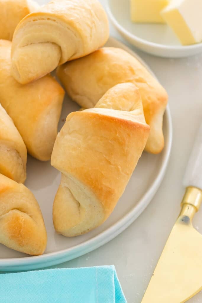 Golden, baked crescent rolls piled on a plate with butter in the background.