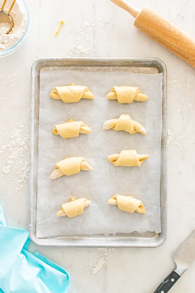 Unbaked crescent rolls arranged on a parchment-lined sheet pan.