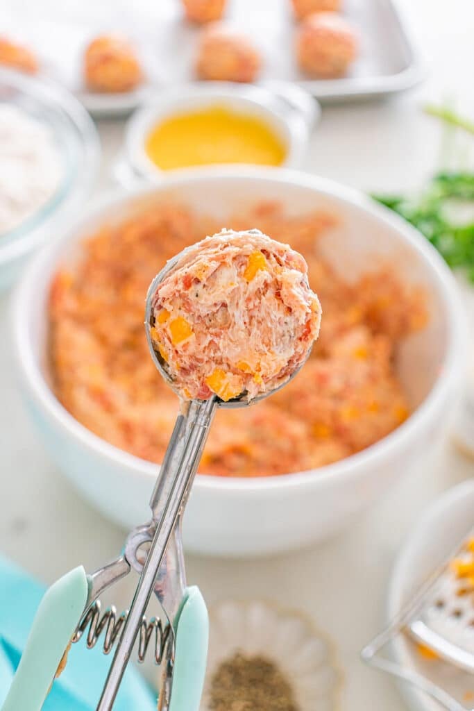 A cookie scoop holding a ball of raw sausage and cheese mixture.