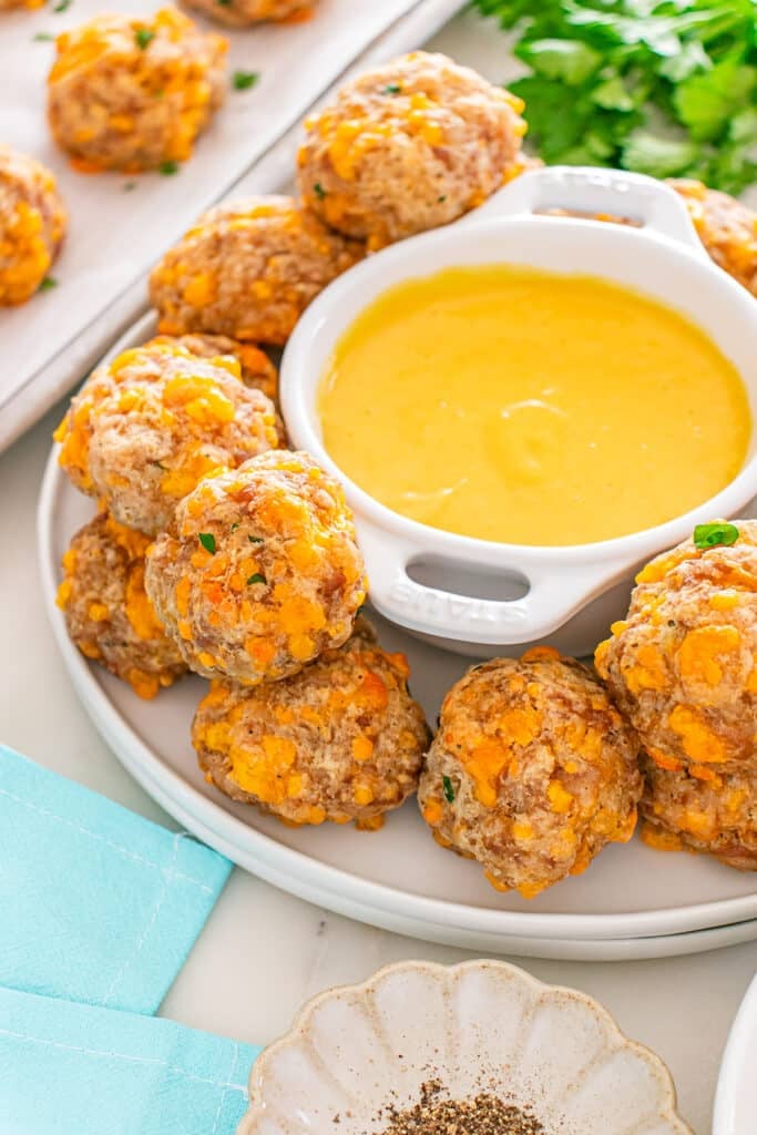 Golden-brown sausage balls stacked around a bowl of creamy yellow dipping sauce.