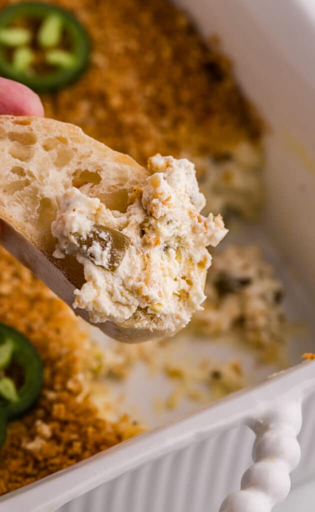 Slice of bread dipped into creamy jalapeño popper dip.