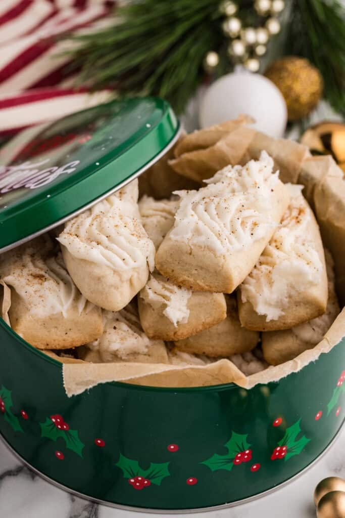 Frosted cookies stacked inside a green holiday tin lined with parchment paper.