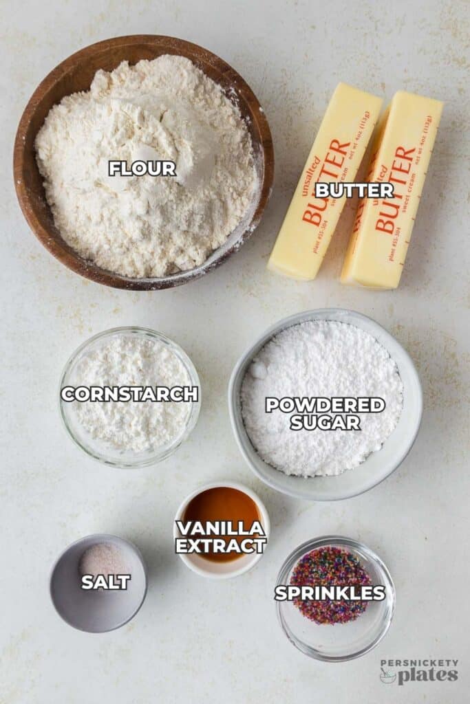 Measured baking ingredients labeled flour, butter, powdered sugar, cornstarch, vanilla extract, salt, and sprinkles.