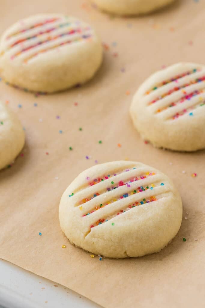 Unbaked shortbread cookies on parchment paper sprinkled with rainbow sprinkles.