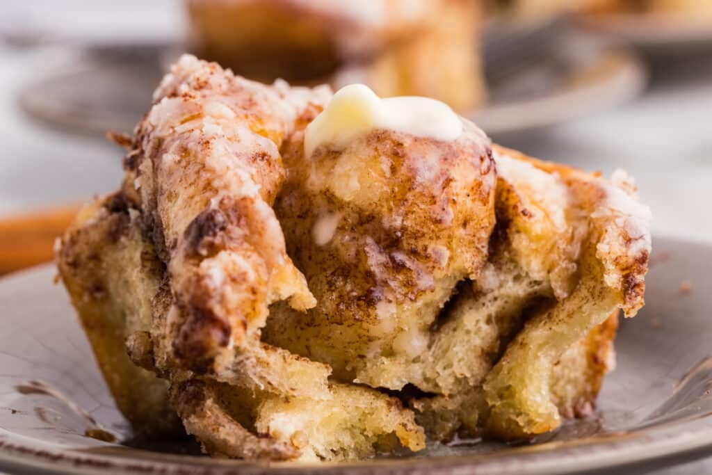Close-up of a torn piece of cinnamon roll on a plate, showing soft interior layers with cinnamon filling and icing on top.