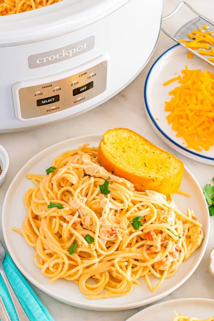 Plate of creamy chicken spaghetti with garlic bread beside a slow cooker.