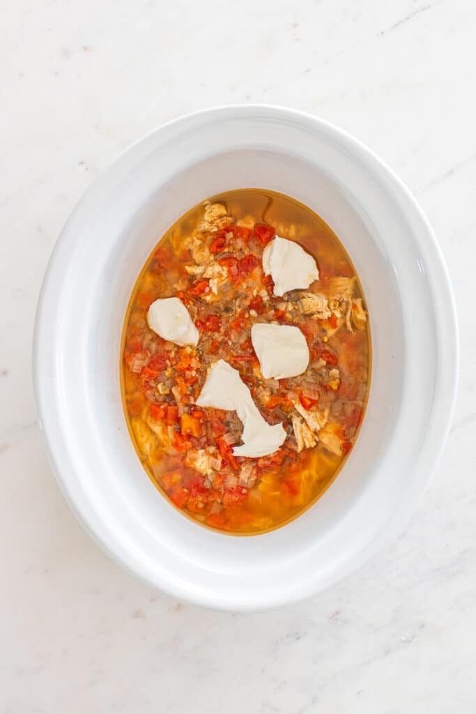 Shredded chicken and diced tomatoes in slow cooker with chunks of cream cheese.