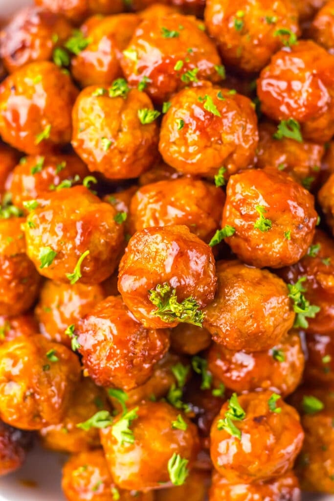 Close-up of glossy meatballs coated in sauce and garnished with chopped parsley.