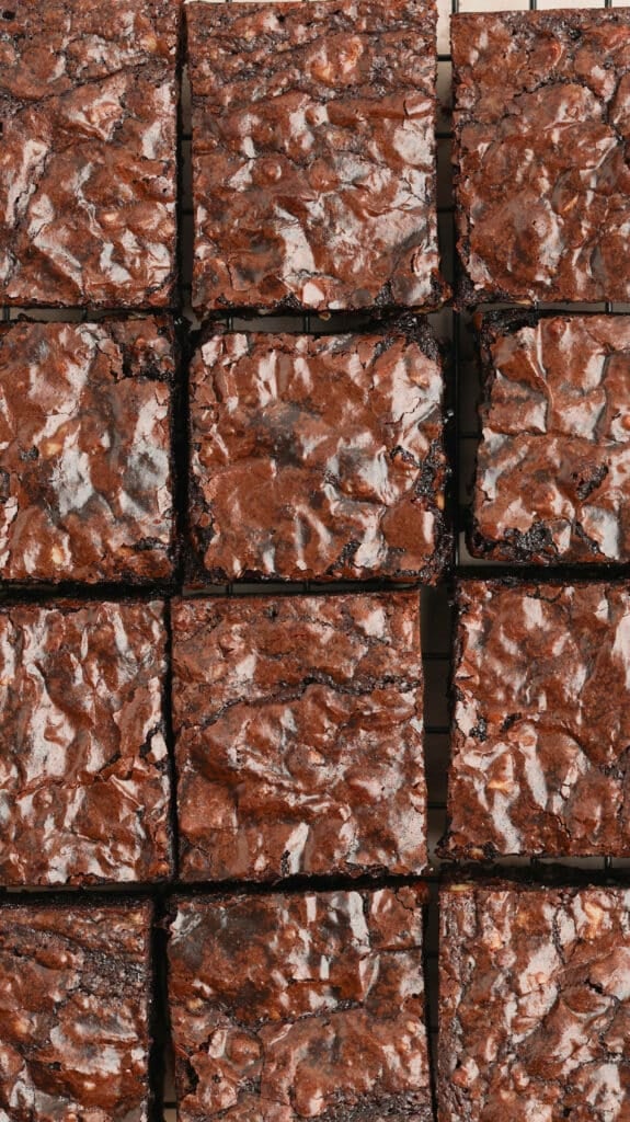 Grid of square chocolate brownies with crackled tops arranged on a cooling rack.