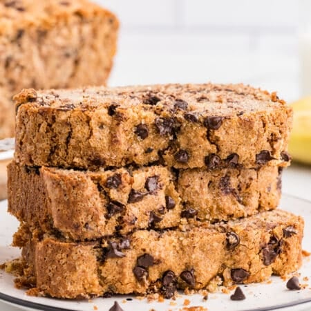 Stacked slices of chocolate chip banana bread on a white plate with chocolate chips and crumbs around the base.