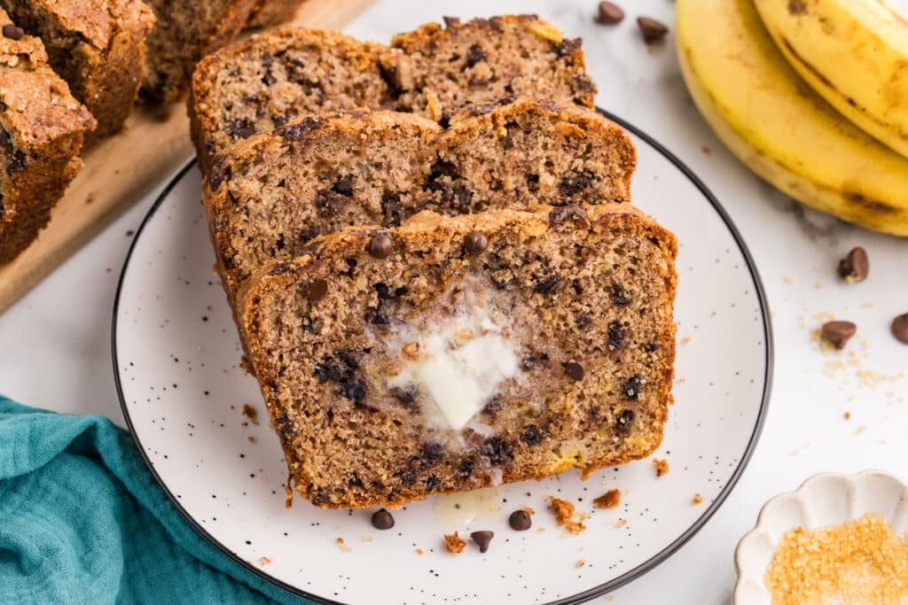 Slices of chocolate chip banana bread on a white plate with a pat of melting butter on the front slice.