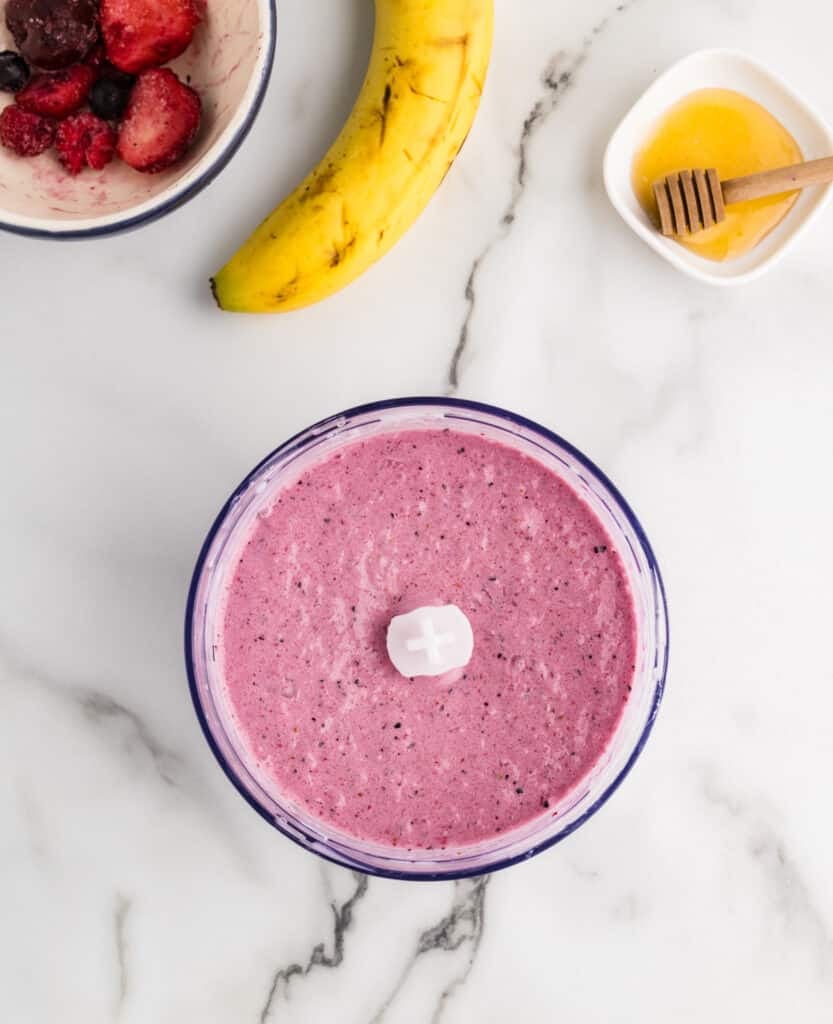 a blended mixed berry smoothie in a blender cup on a marble countertop.