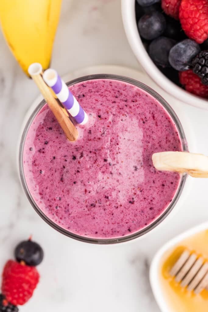 Overhead view of a mixed berry smoothie in a glass with paper straws and a banana slice garnish.