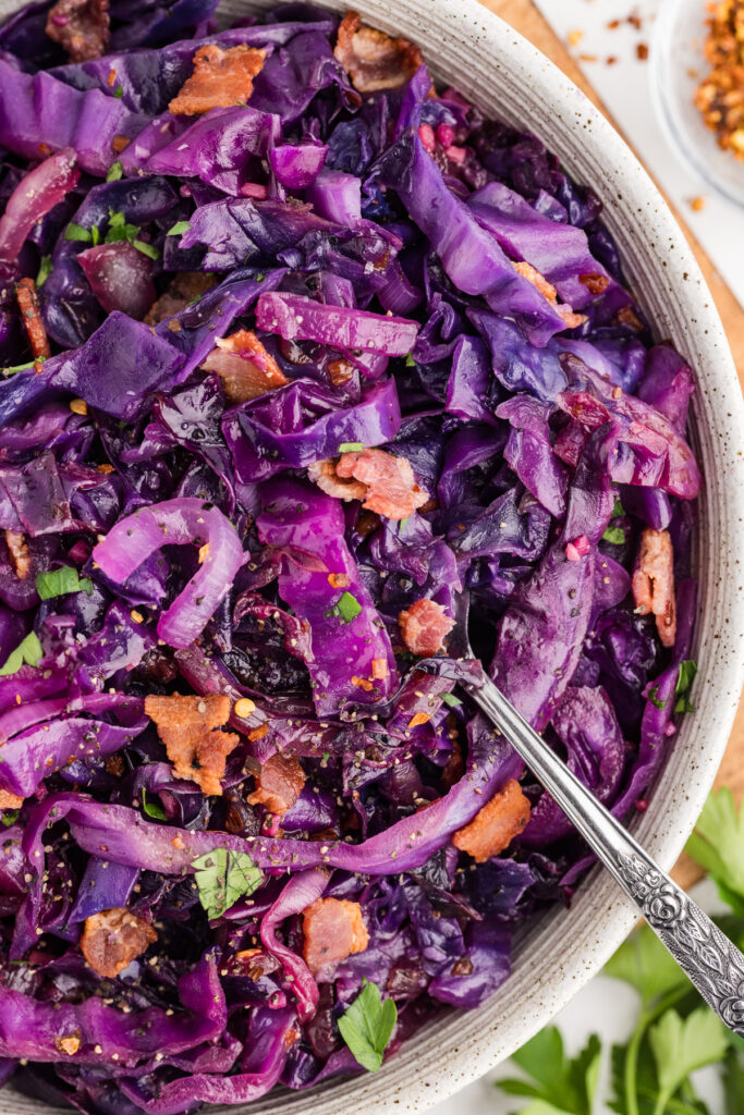 Close-up of stir fried red cabbage with bacon and onions in a bowl with a spoon.