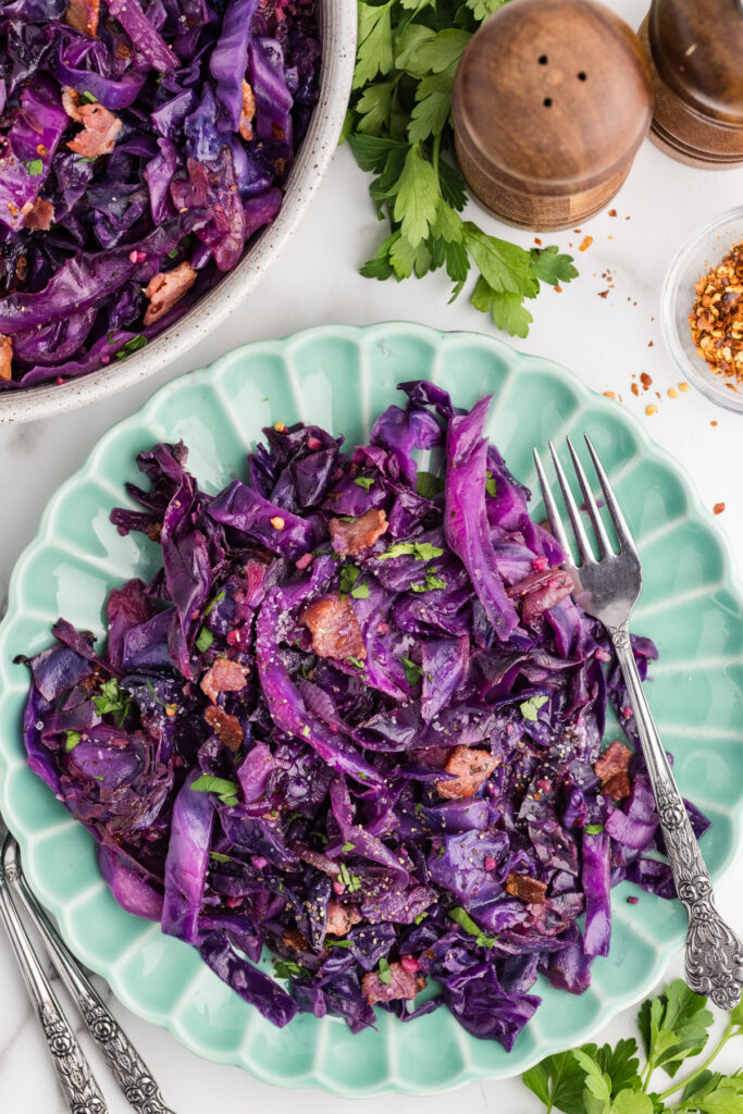 Stir fried red cabbage with bacon and parsley served on a green plate with a fork.