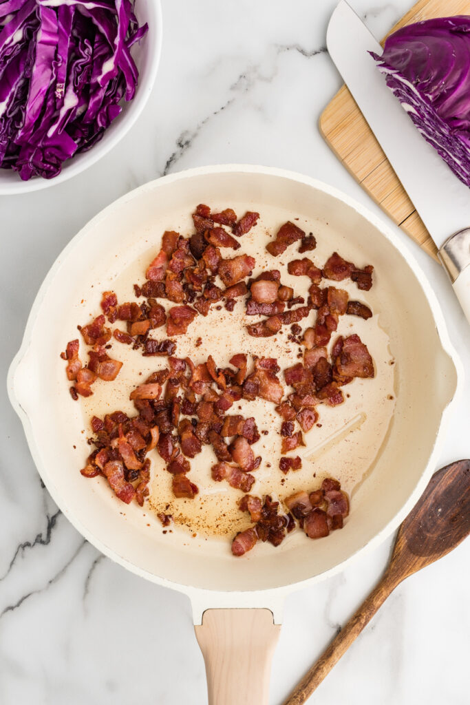 Crispy chopped bacon cooking in a skillet with rendered fat.