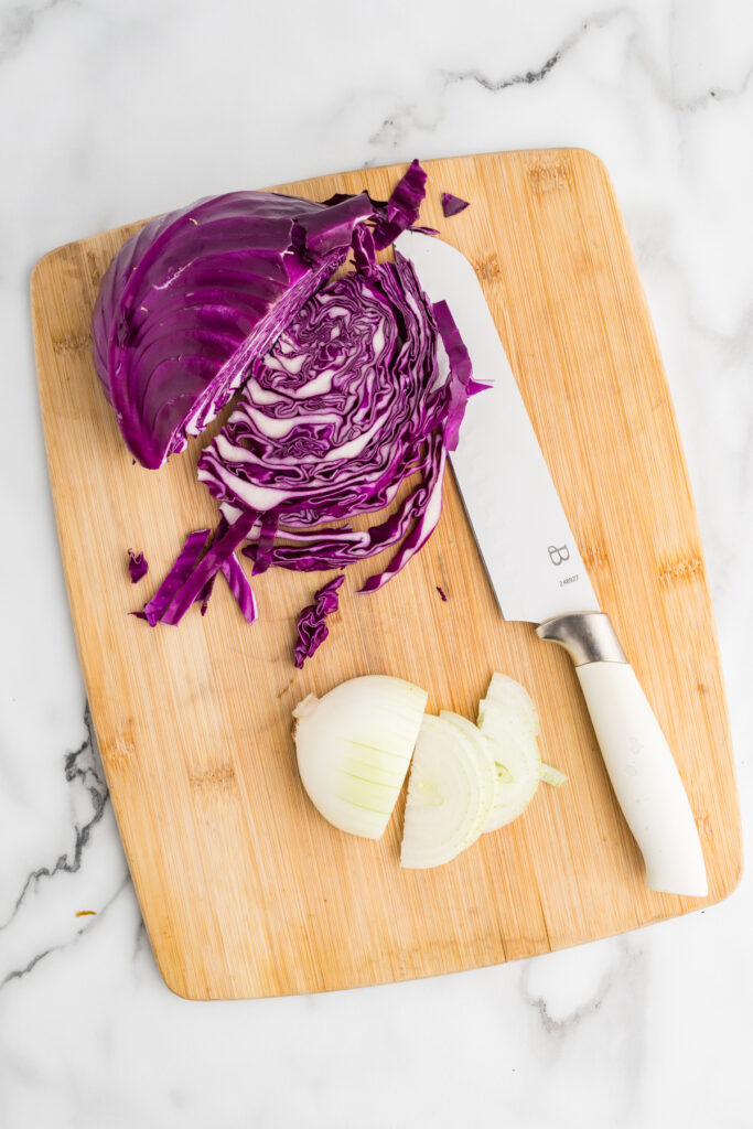 Chopped red cabbage and sliced onion on a cutting board with a knife.