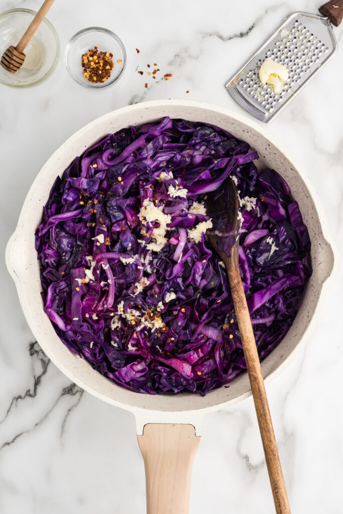 Stir fried red cabbage with garlic and red pepper flakes in a skillet with a wooden spoon.