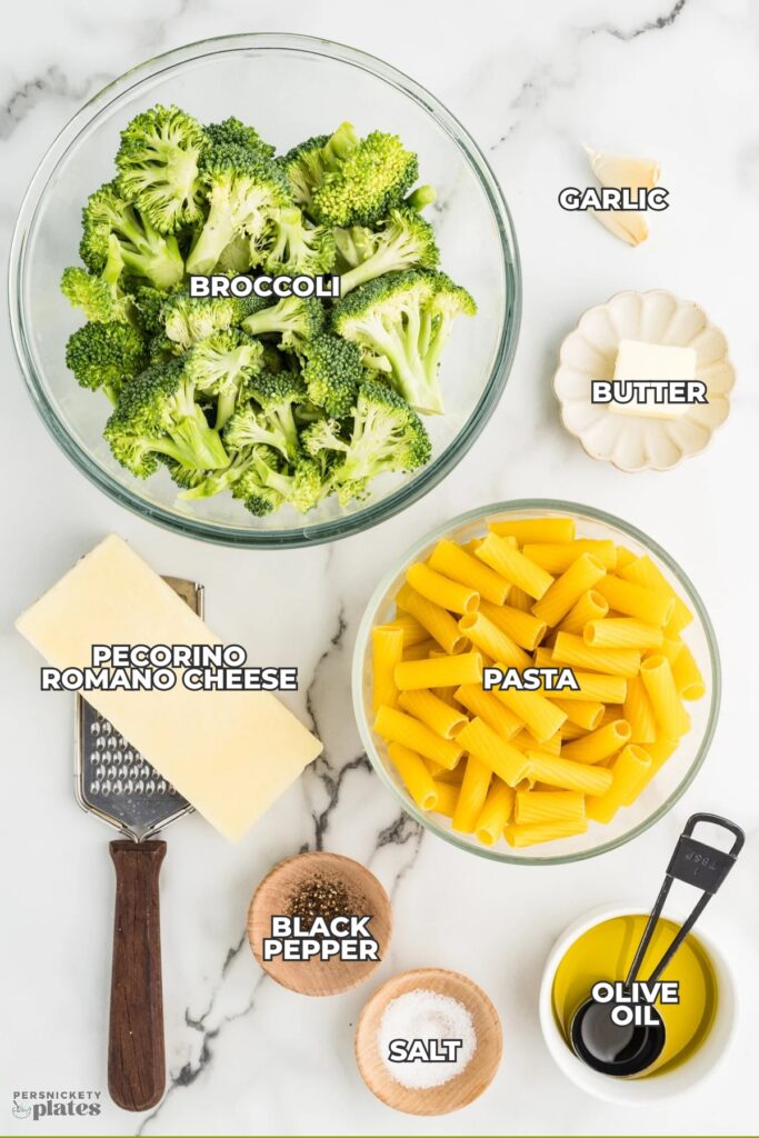 Top-down view of labeled ingredients laid out to make broccoli pasta on a light marble surface.