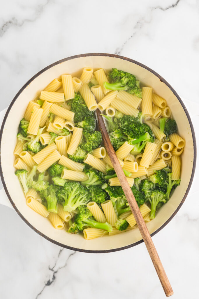 Rigatoni pasta and broccoli being stirred in a pot with a wooden spoon.