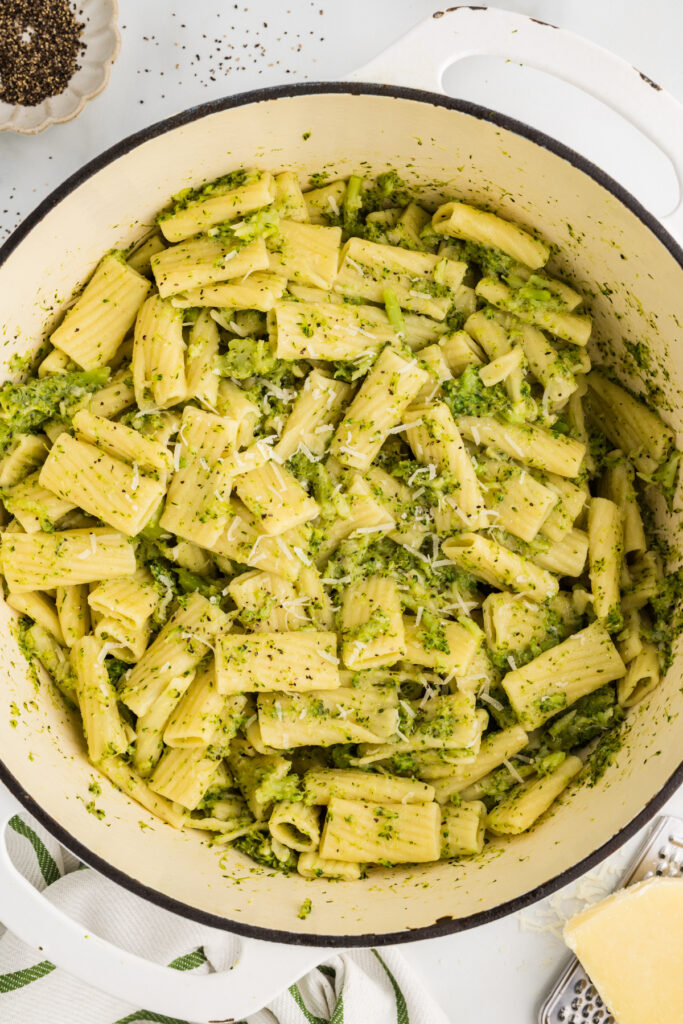 a large pot filled with rigatoni pasta tossed with chopped broccoli, grated cheese, and black pepper, lightly coated in a green-tinted sauce.