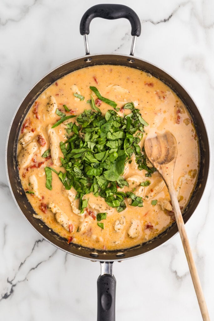Chopped greens added to creamy chicken sauce in a skillet