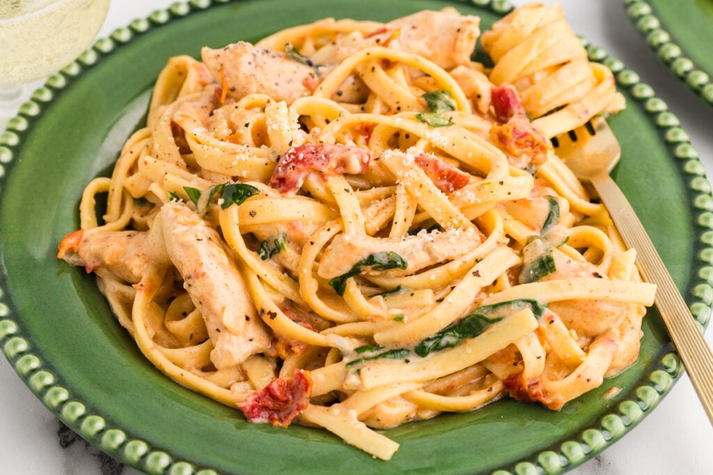Chicken pasta with sun-dried tomatoes on a green plate..
