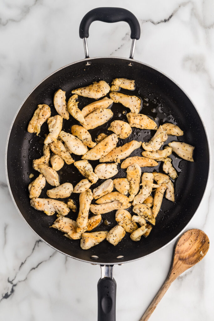 Cooked chicken pieces in a skillet on a marble surface