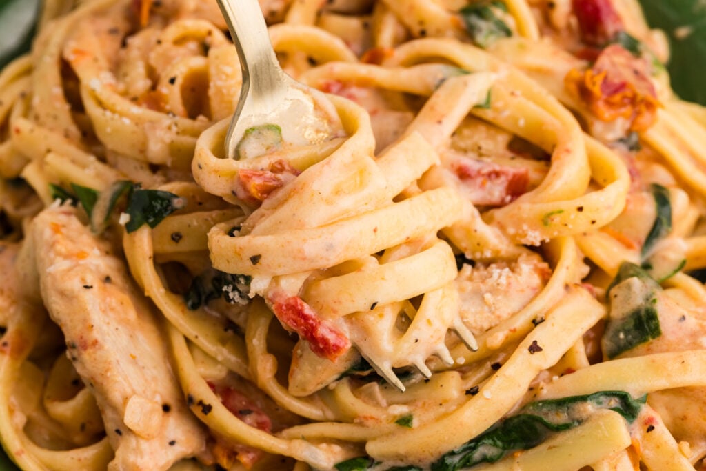 Fork lifting creamy chicken pasta with sun-dried tomatoes.