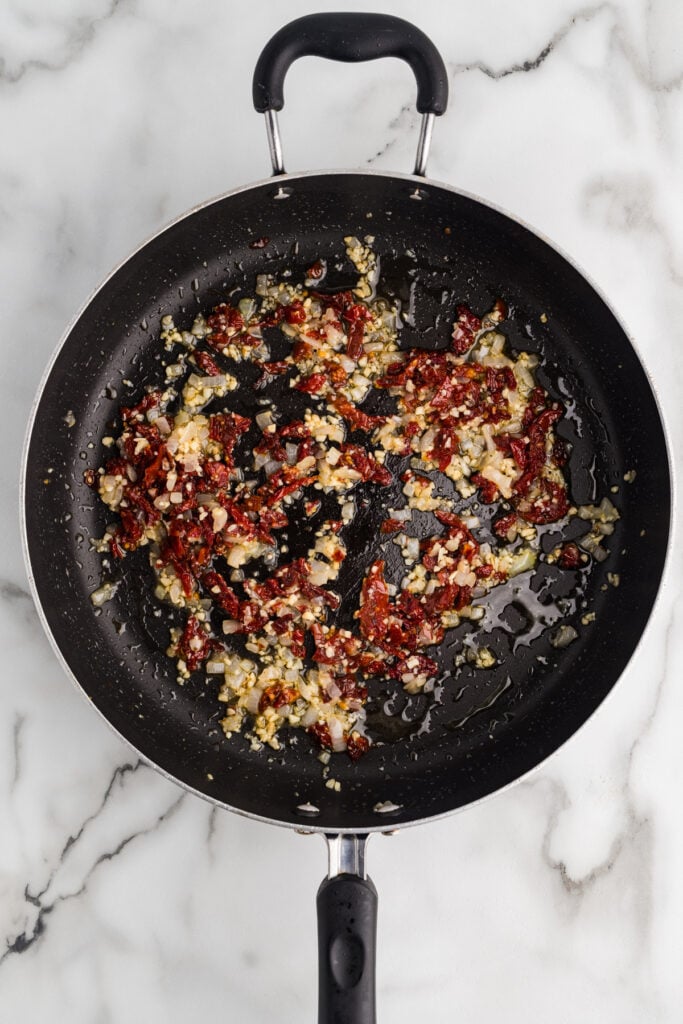 Sun-dried tomatoes, garlic, and onions cooking in a skillet