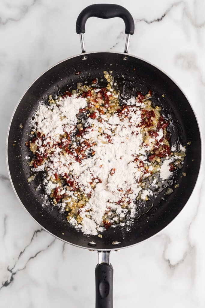 Flour added to sun-dried tomatoes and garlic in a skillet