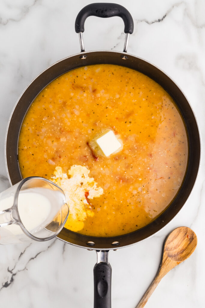 Cream being poured into a skillet with sauce and butter