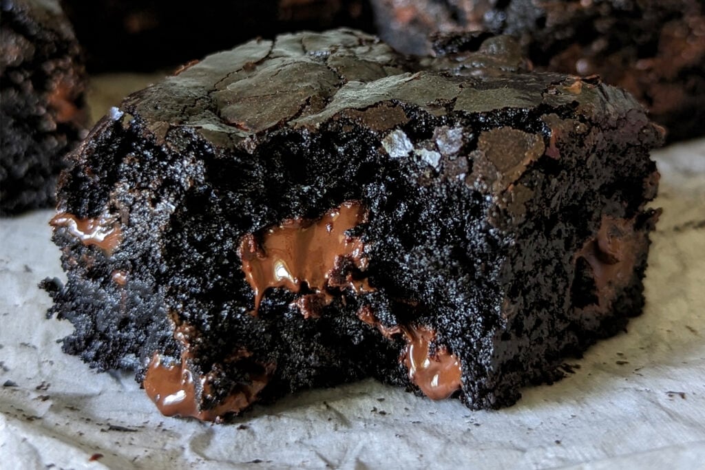 a single black cocoa brownie with a bite missing and a melty chocolate chip inside.