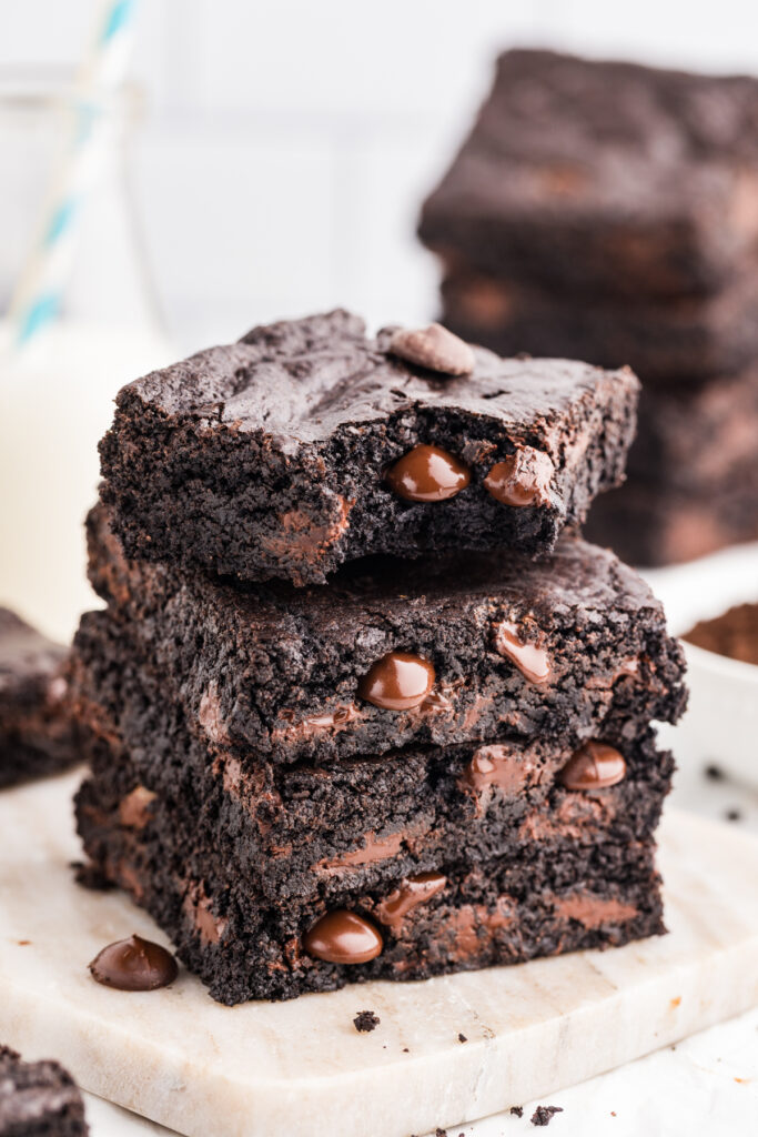Stack of dark chocolate brownies with melted chocolate chips on a marble board.