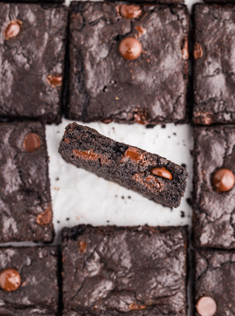 Overhead view of dark cocoa brownies with one brownie turned on its side showing the fudgy center.