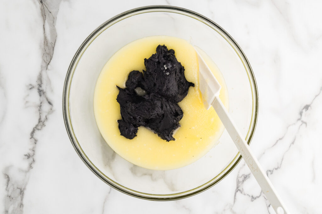 Black cocoa mixture on top of melted butter in a glass mixing bowl with a white spatula.