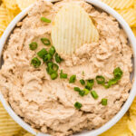 Creamy French onion dip topped with green onions and served with potato chips.