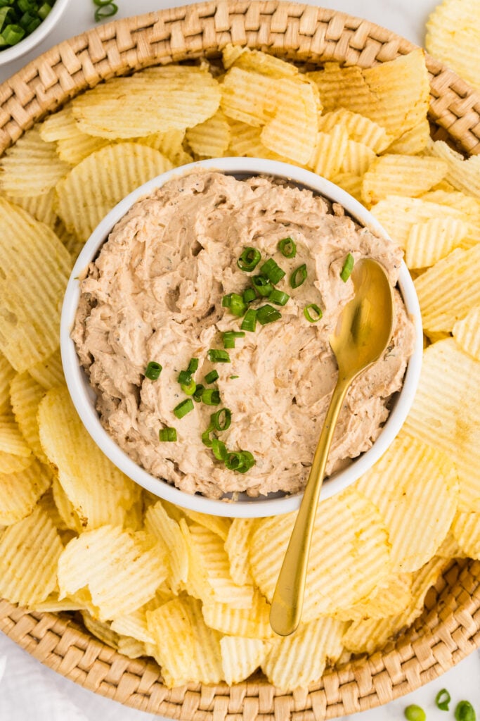 Bowl of French onion dip surrounded by ridged potato chips on a woven tray.