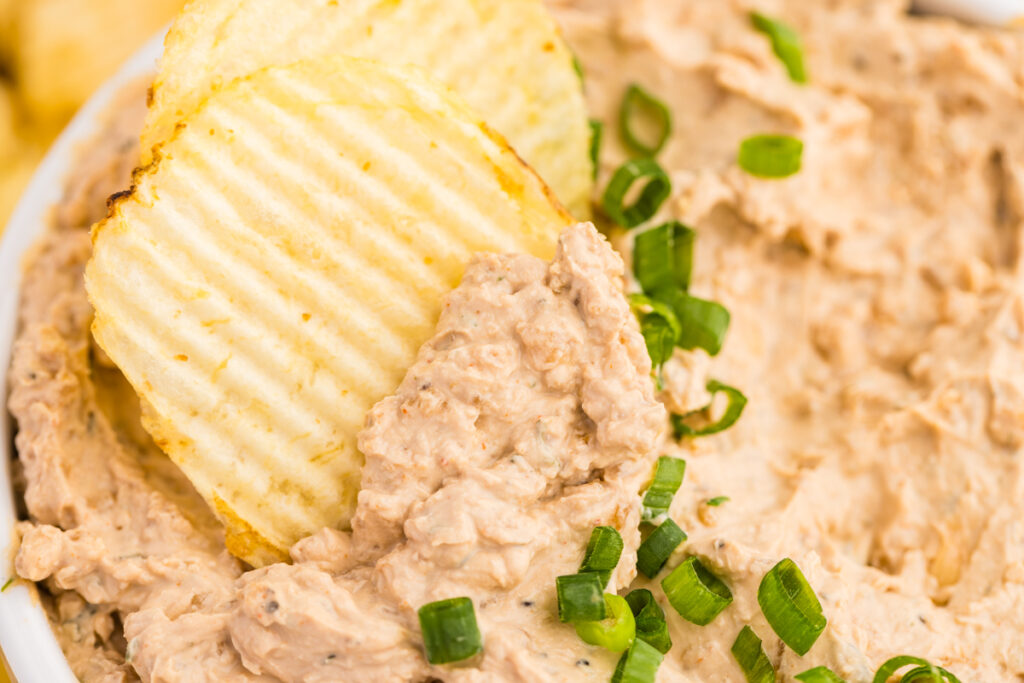 Ridged potato chips dipped into a bowl of creamy French onion dip topped with sliced green onions.
