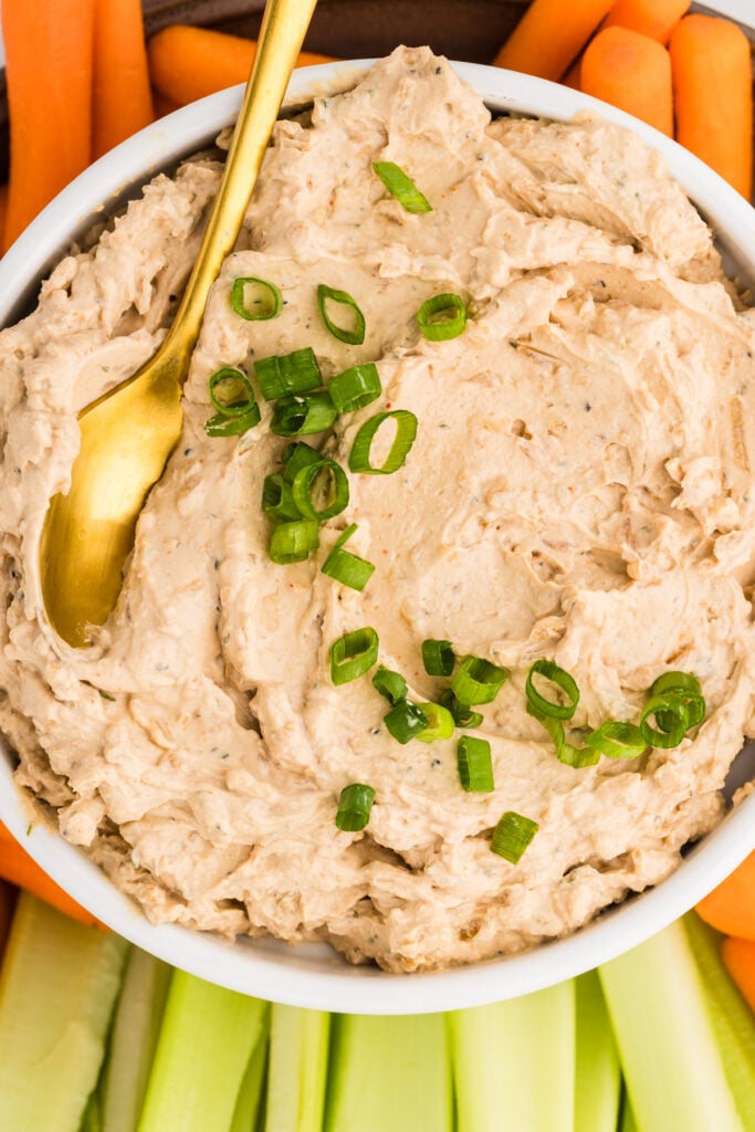 Bowl of creamy French onion dip topped with green onions and served with carrots and celery.