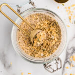Gold measuring spoon scooping homemade onion soup mix from a glass jar.