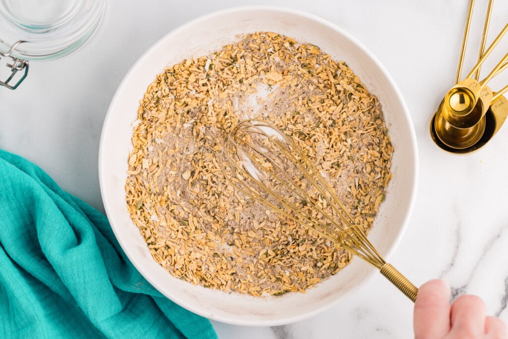 Homemade onion soup mix ingredients being whisked in a white bowl.