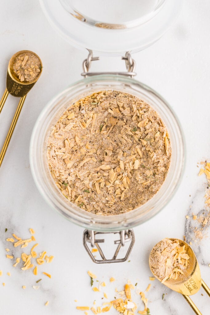 Glass jar filled with homemade onion soup mix beside gold measuring spoons.