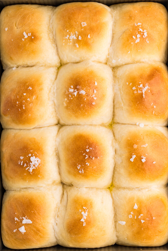 Pan of golden brown potato dinner rolls topped with flaky salt.