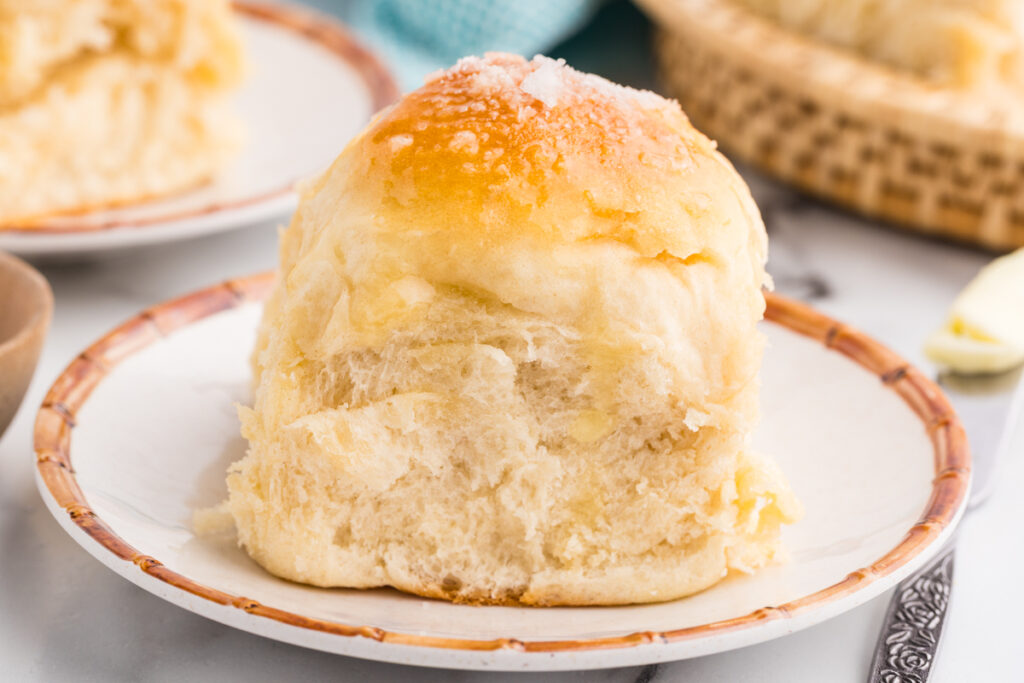 Single potato dinner roll on a plate with a soft, fluffy interior.