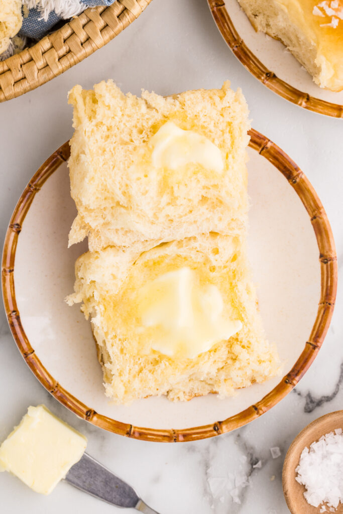Two potato dinner rolls split and stacked with melting butter on a plate.