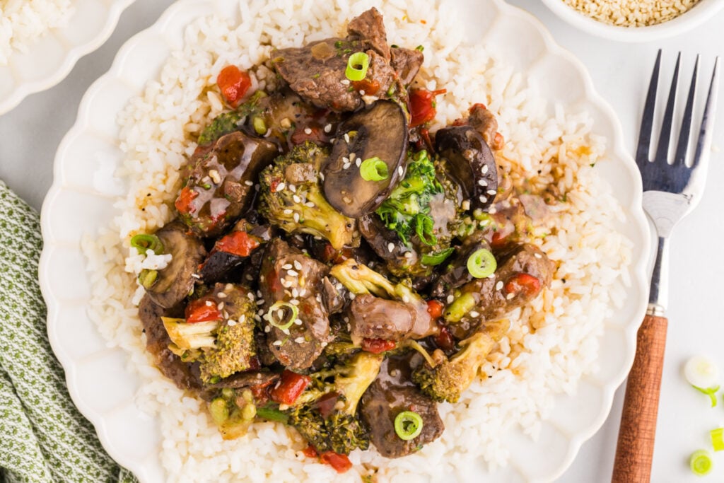 Slow cooker pepper steak with broccoli, mushrooms, and red peppers served over white rice.