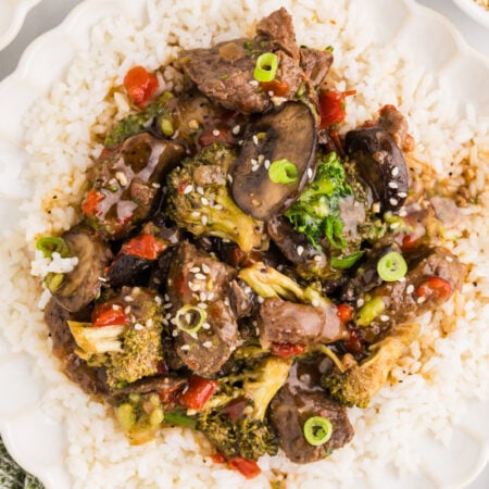 Close-up of slow cooker pepper steak with broccoli, mushrooms, and red peppers served over white rice.